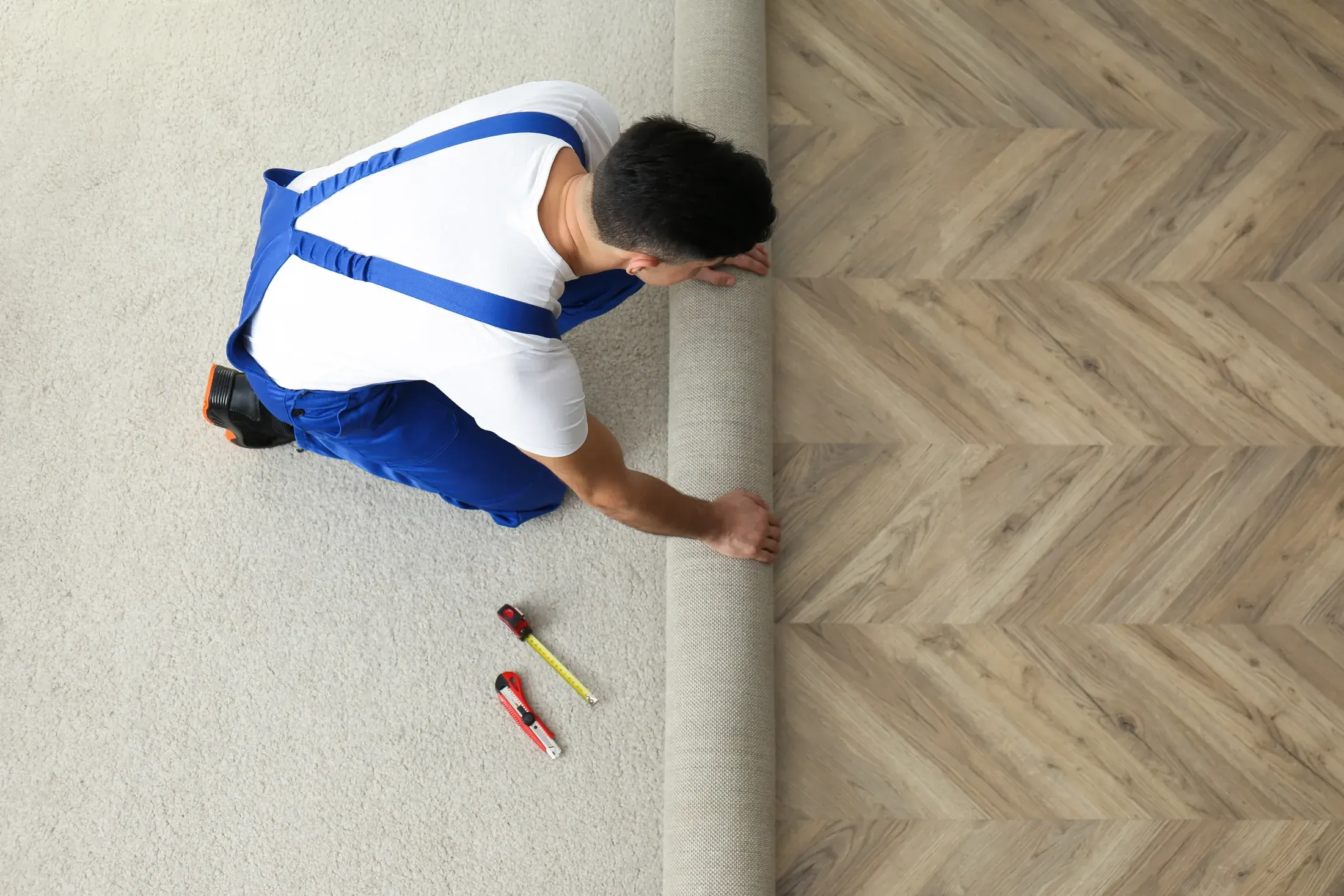 Installer unrolling new carpet next to an existing herringbone wood floor