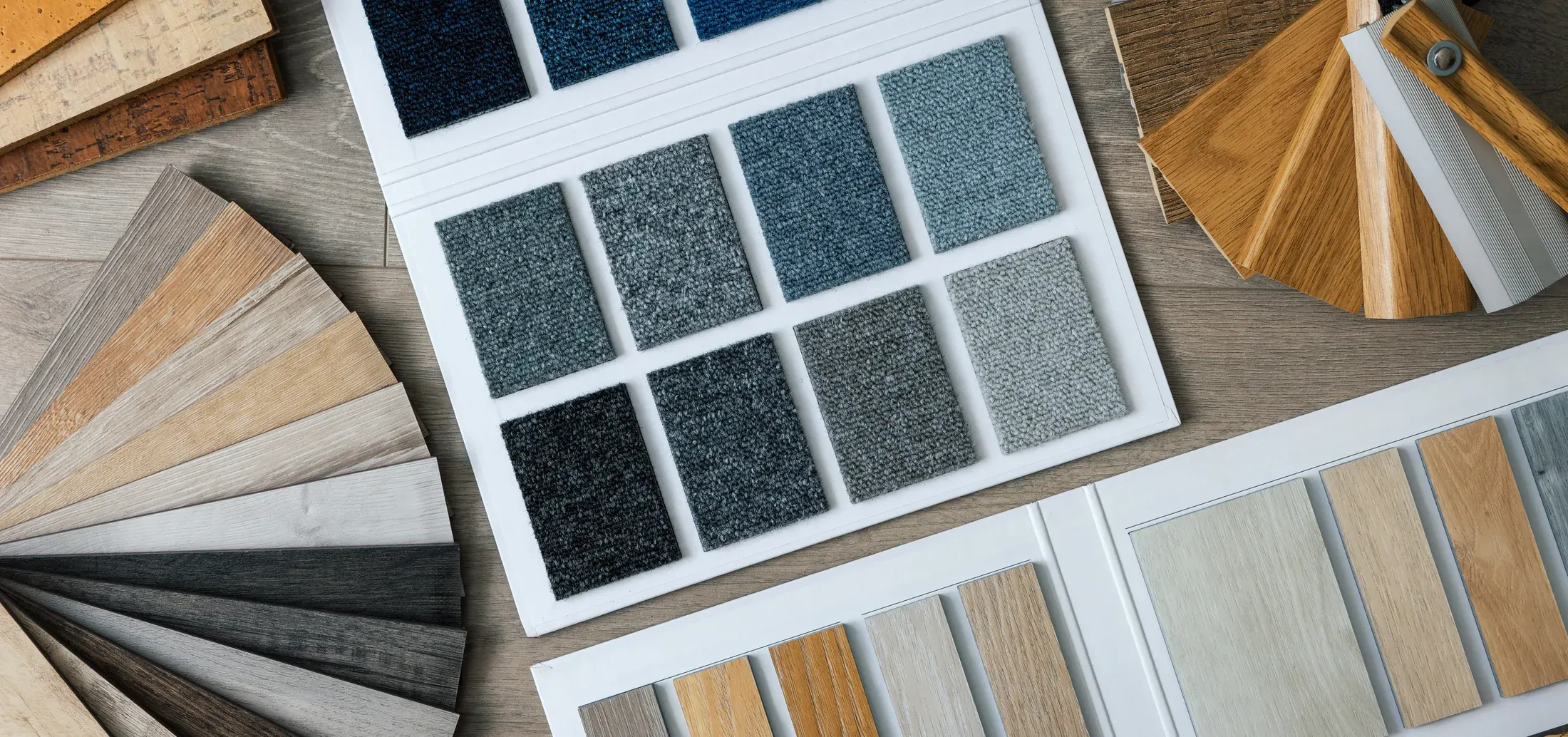 Overhead flat-lay of carpet, wood, and laminate flooring material samples fanned out for comparison