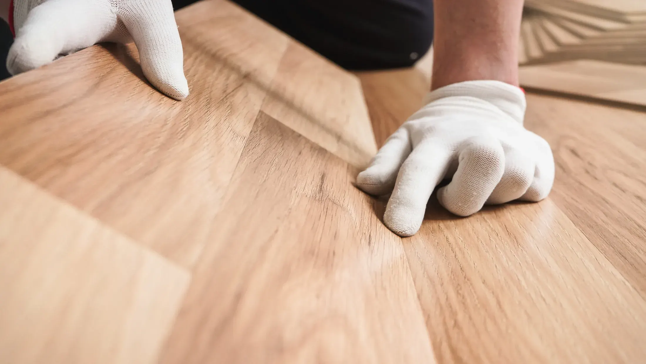 Close-up of gloved hands fitting a laminate flooring plank into place during installation