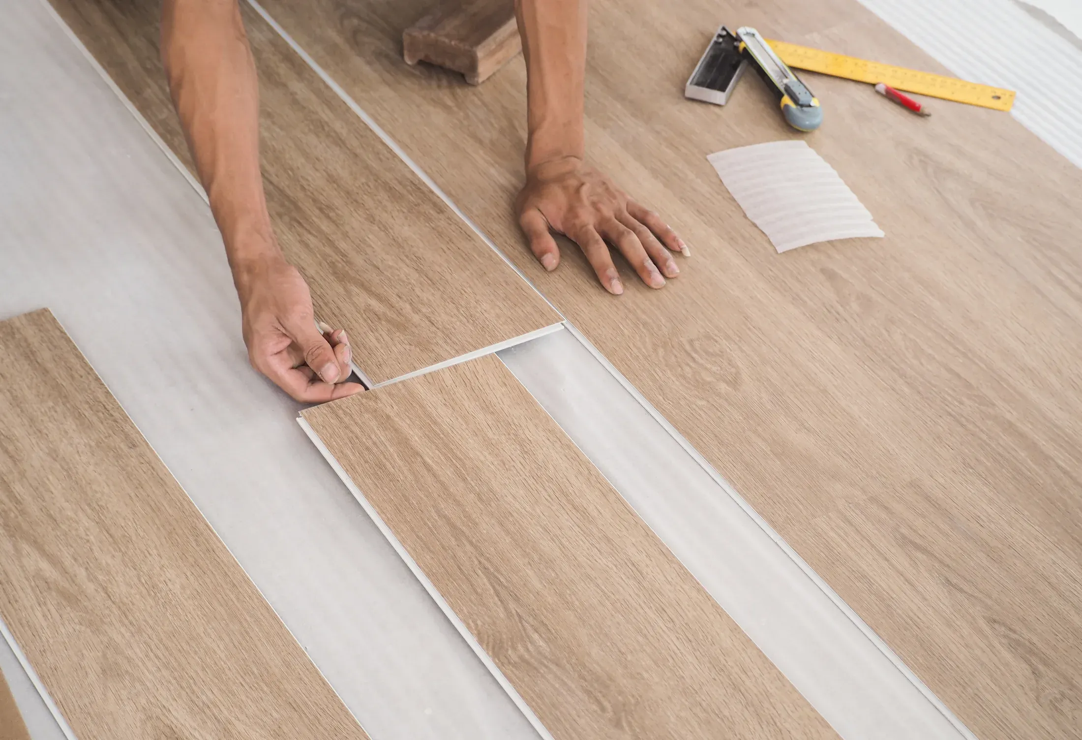 Close-up of hands fitting a luxury vinyl plank into place during installation